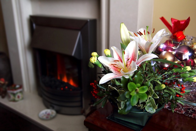 Lovely festive Christmas flower arrangement with lilies and carnations, fireplace in background, copy space for text