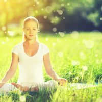 young woman enjoying meditation and yoga on green grass in summer on nature