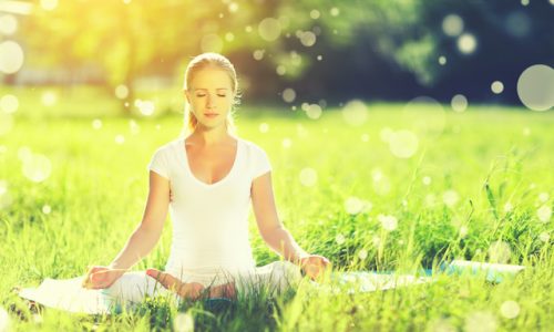 young woman enjoying meditation and yoga on green grass in summer on nature