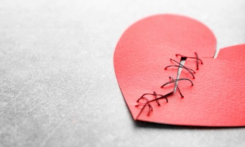 愛・復活愛Paper heart cut in half and sewn back together on light background. Relationship problems